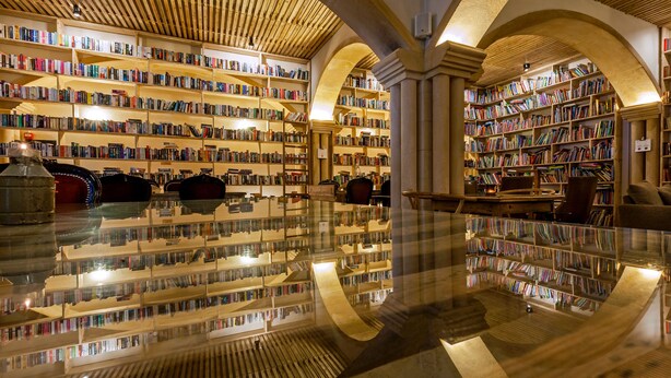 Una biblioteca amplia con techos altos, numerosas estanterías y un suelo pulido que refleja los libros y los muebles.