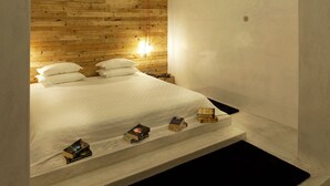Un dormitorio con techo de madera, una cama con ropa de cama blanca y un estante pequeño con libros.