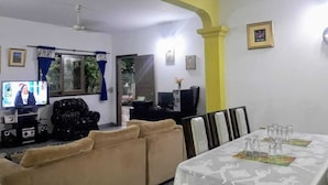 A living room with a sofa, a dining table with chairs, a television, and a ceiling fan. - Nueva Alborada Lodging House (Fernando De La Mora)