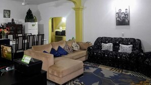 A living room with a beige sofa, a black patterned sofa, and a coffee table. There is a dining area in the background with a white refrigerator and a Christmas tree. - Nueva Alborada Lodging House (Fernando De La Mora)