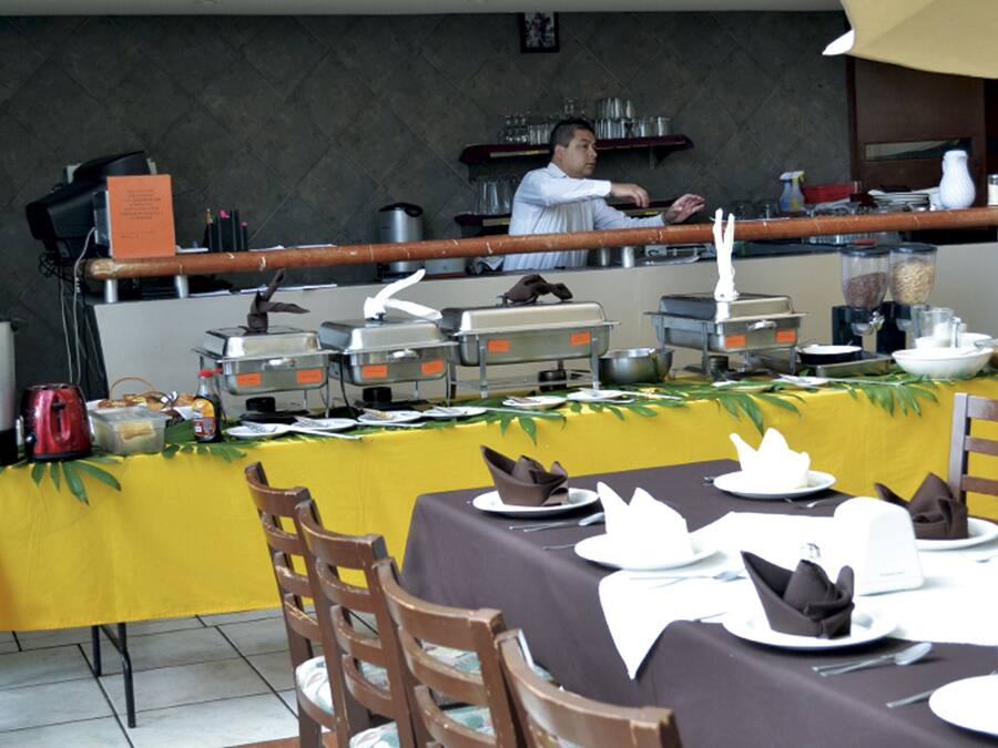 En buffé med flera serveringsstationer, en kock som tillagar maten och ett bord täckt med en gul duk, där tallrikar och servetter är prydligt upplagda.