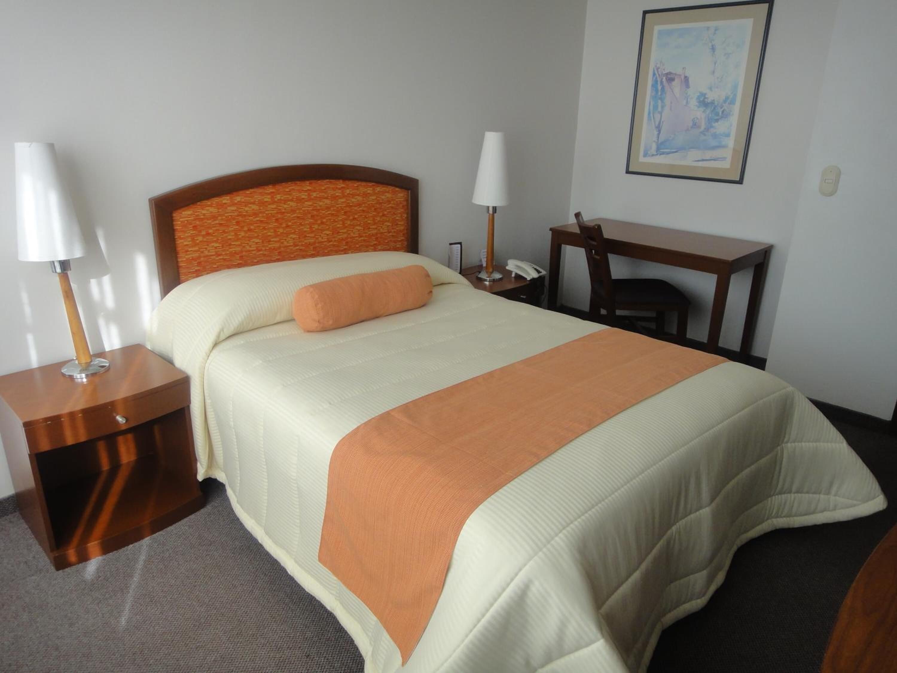Een netjes ingerichte hotelkamer met een bed, nachtkastjes, een bureau en een stoel.