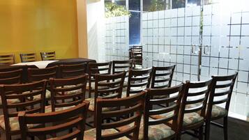 Un salón de conferencias con una gran mesa y varias sillas, una pared amarilla y un ventanal con vistas a árboles.