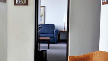 Un pasillo de hotel con suelo de baldosas, un sofá azul, una mesa de madera y un cuadro en la pared.