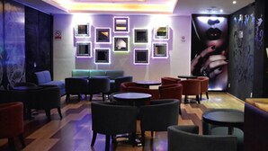 Ein stilvoller Lounge-Bereich mit verschiedenen Sitzgelegenheiten, darunter Sofas und runden Tischen, einem gemusterten Boden und dekorativer Wandbeleuchtung.