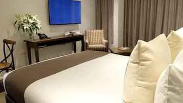 Una habitación de hotel con una cama grande, un escritorio con teléfono, una silla, un televisor montado en la pared y una ventana con cortinas.