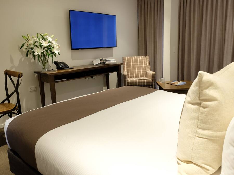 Una habitación de hotel con una cama grande, un escritorio con teléfono, una silla, un televisor montado en la pared y una ventana con cortinas.