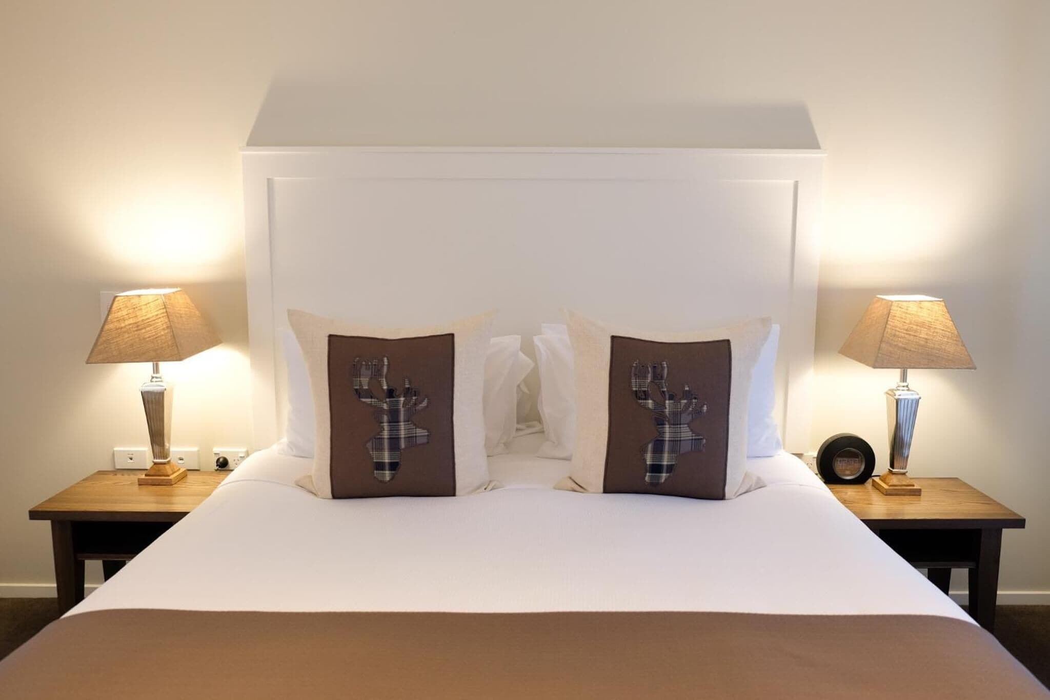 Una camera d'albergo con un letto grande, due comodini, due lampade e cuscini decorativi con motivi di renne.