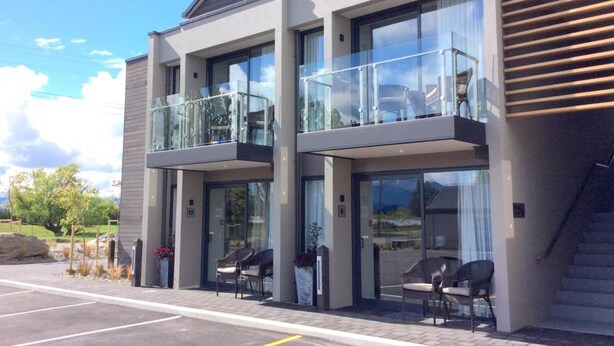 A modern building with a glass balcony, a parking lot, and outdoor seating. - West Meadows Motel (Wanaka)