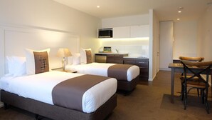 A hotel room with two beds, a desk, and a kitchenette. - West Meadows Motel (Wanaka)