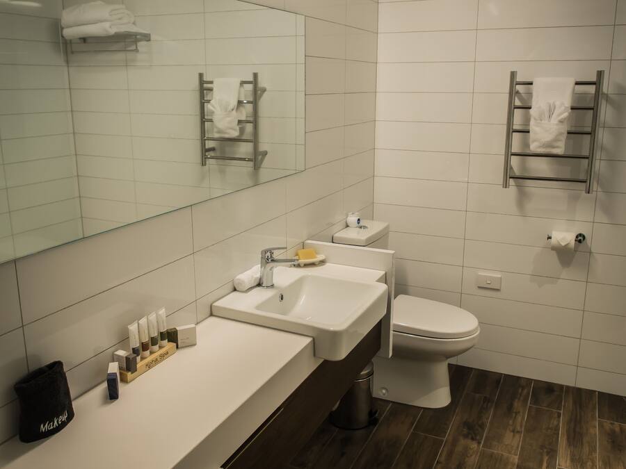 Un baño moderno con lavamanos, espejo y retrete blancos. Hay toallas y artículos de aseo en la encimera.