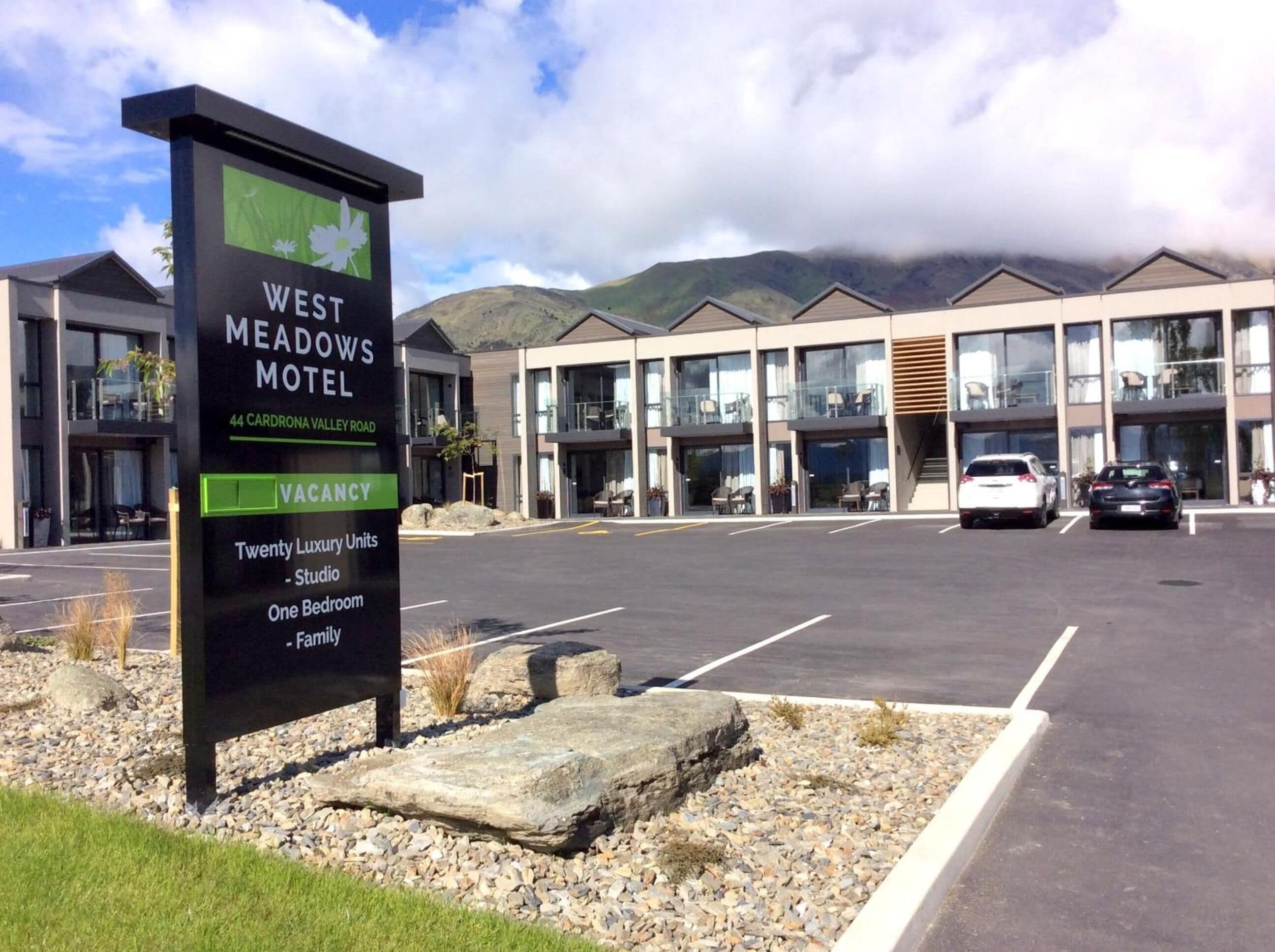 Une enseigne indiquant le « West Meadows Motel » et faisant la publicité de 20 chambres de luxe, dont des studios, des chambres à une chambre et des chambres familiales.