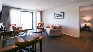 A hotel room with a dining area, a sofa, a chair, a small table, a lamp, and a bed. - West Meadows Motel (Wanaka)