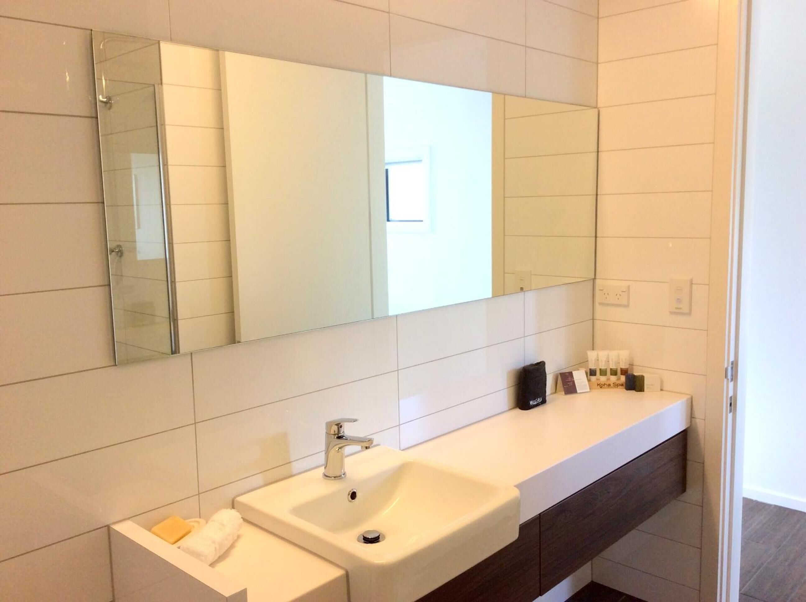 Een moderne badkamer met een grote spiegel, een witte wastafel en een meubel met toiletartikelen.
