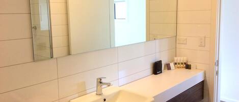 Un baño moderno con un espejo grande, un lavamanos blanco y un mueble de tocador con artículos de aseo.