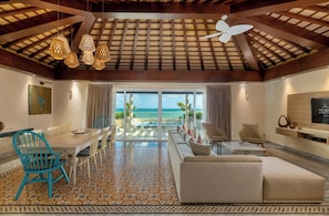Amplia habitación con un ventanal grande con vista al océano, un comedor con mesa y sillas, y una zona de estar con sofá y sillones.