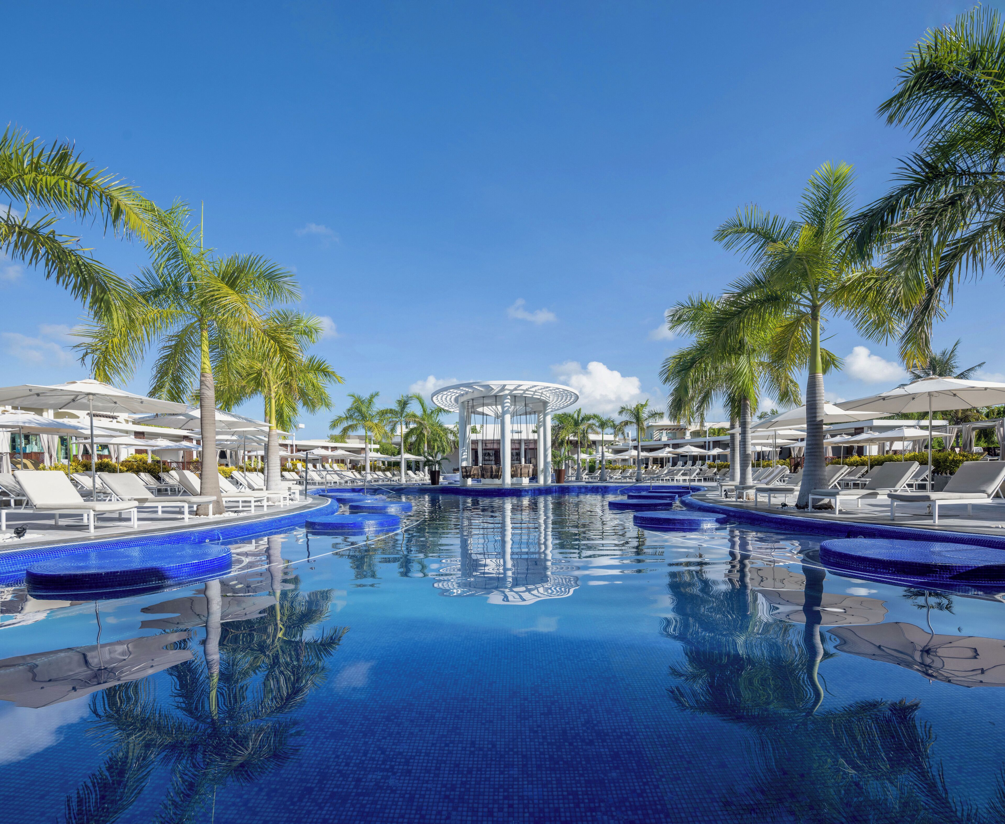 A resort pool with lounge chairs, palm trees, and a central gazebo.
