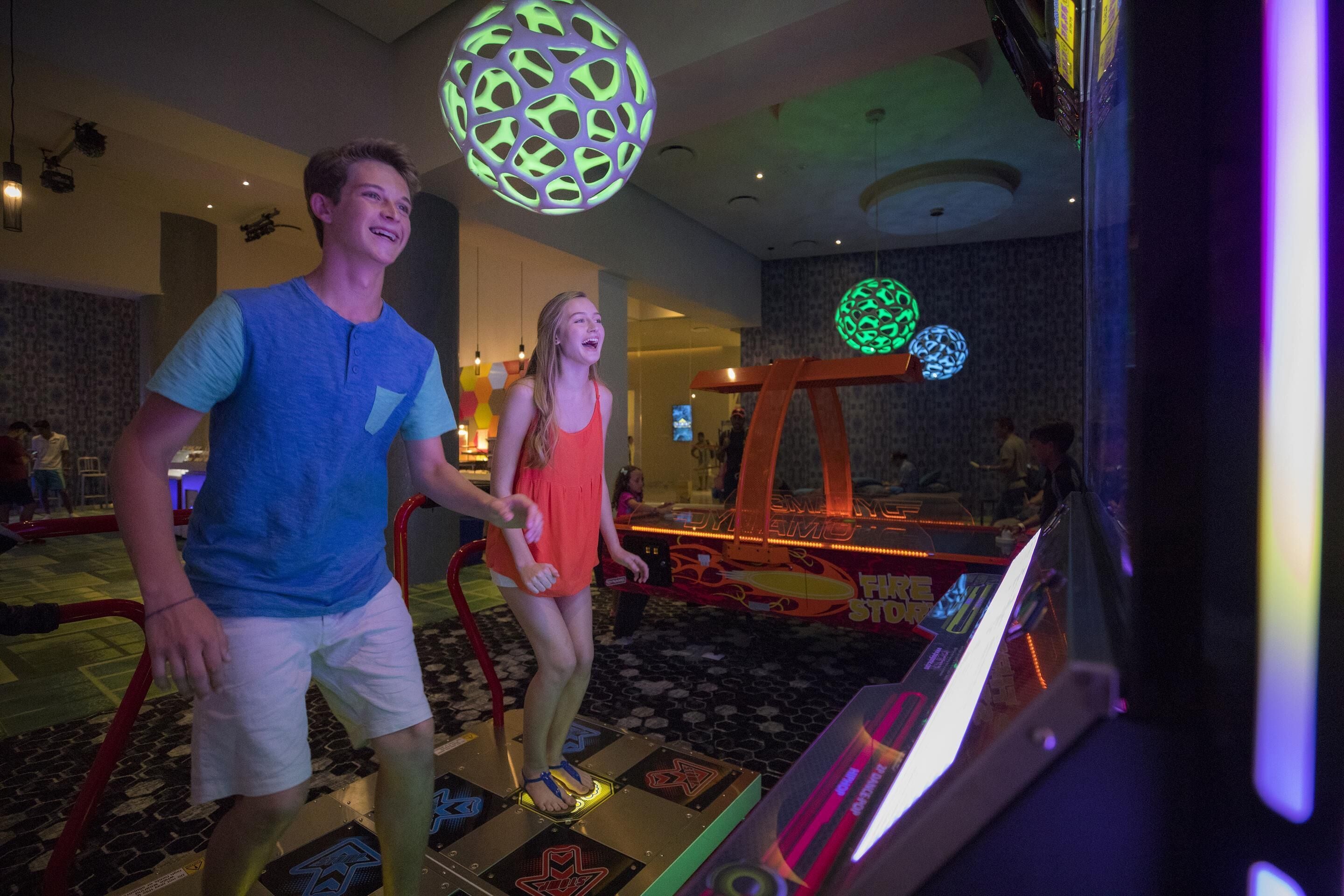 A man and a woman standing on a dance floor with a disco ball overhead and a neon sign in the background.