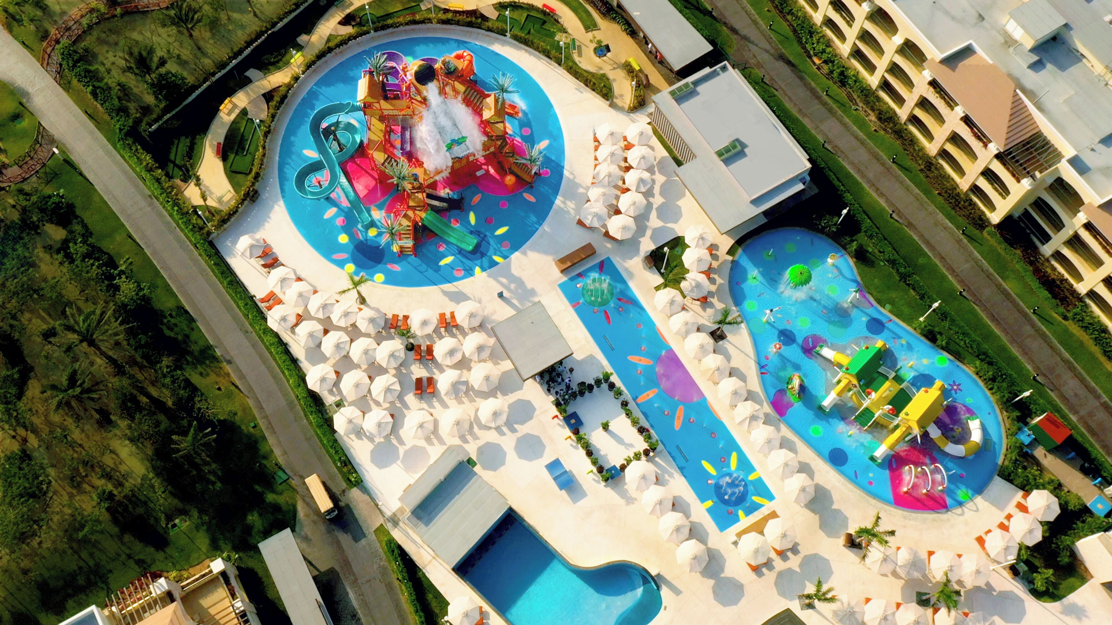 An aerial view of a resort with a large pool area, multiple water slides, and sun loungers.