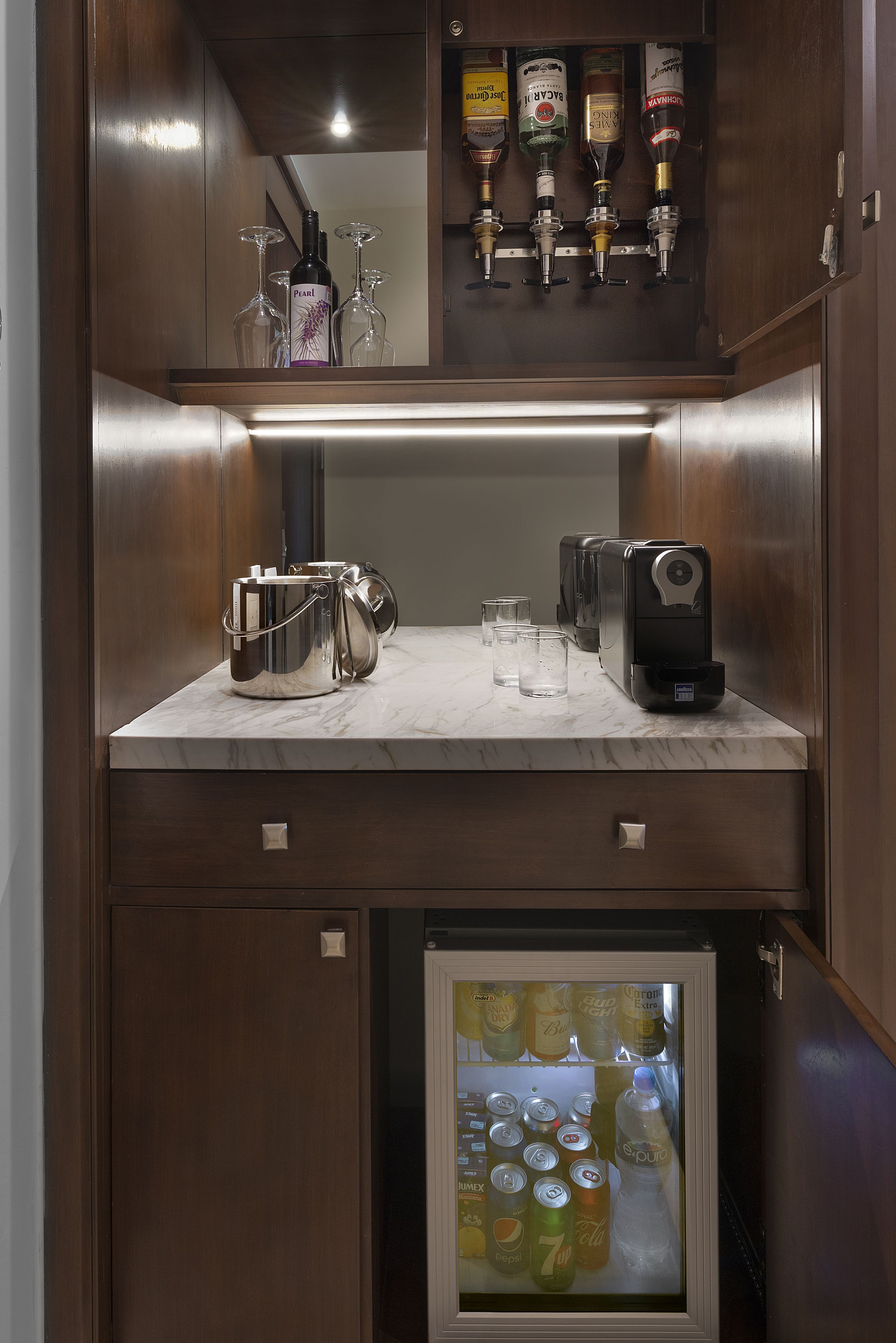 Un minibar compatto con una macchina da caffè, una bottiglia d'acqua e un frigorifero fornito di bevande.