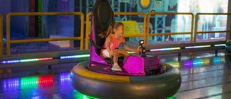 A child in a colorful bumper car at an indoor amusement park.