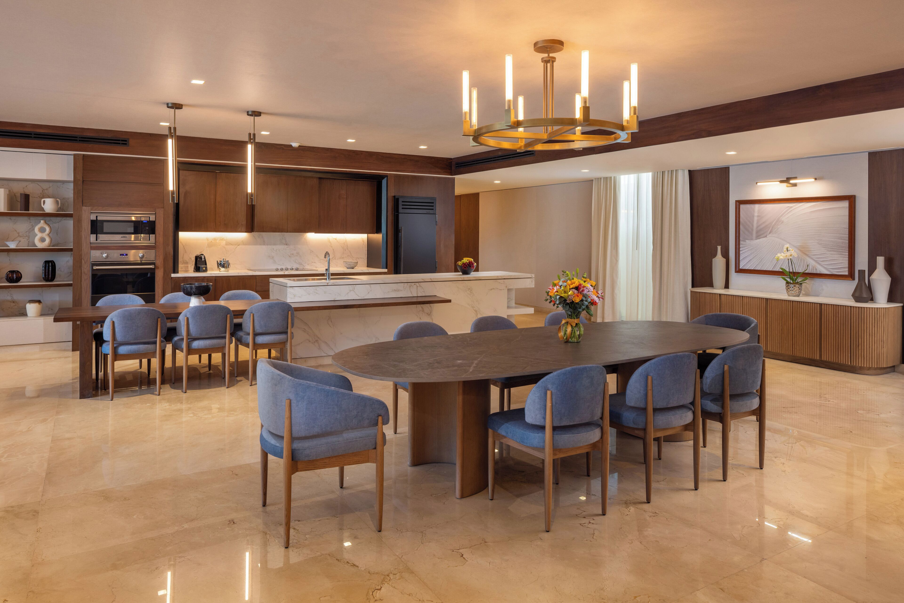 A modern kitchen with built-in appliances, a dining area with a large oval table, and a chandelier.