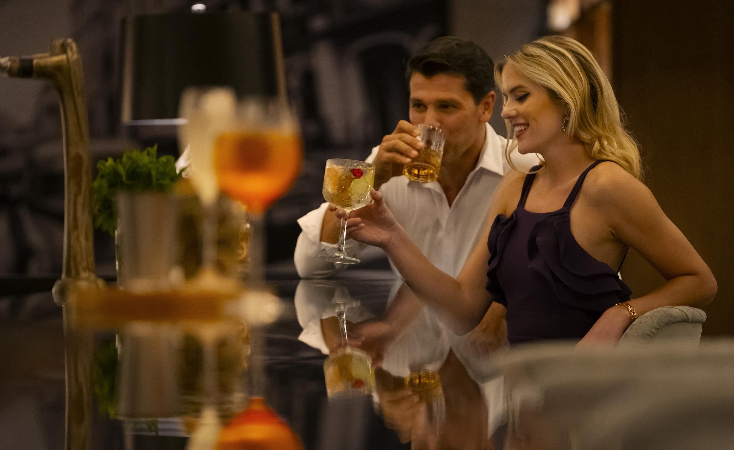 A couple sitting at a table with drinks, in a dimly lit indoor setting.