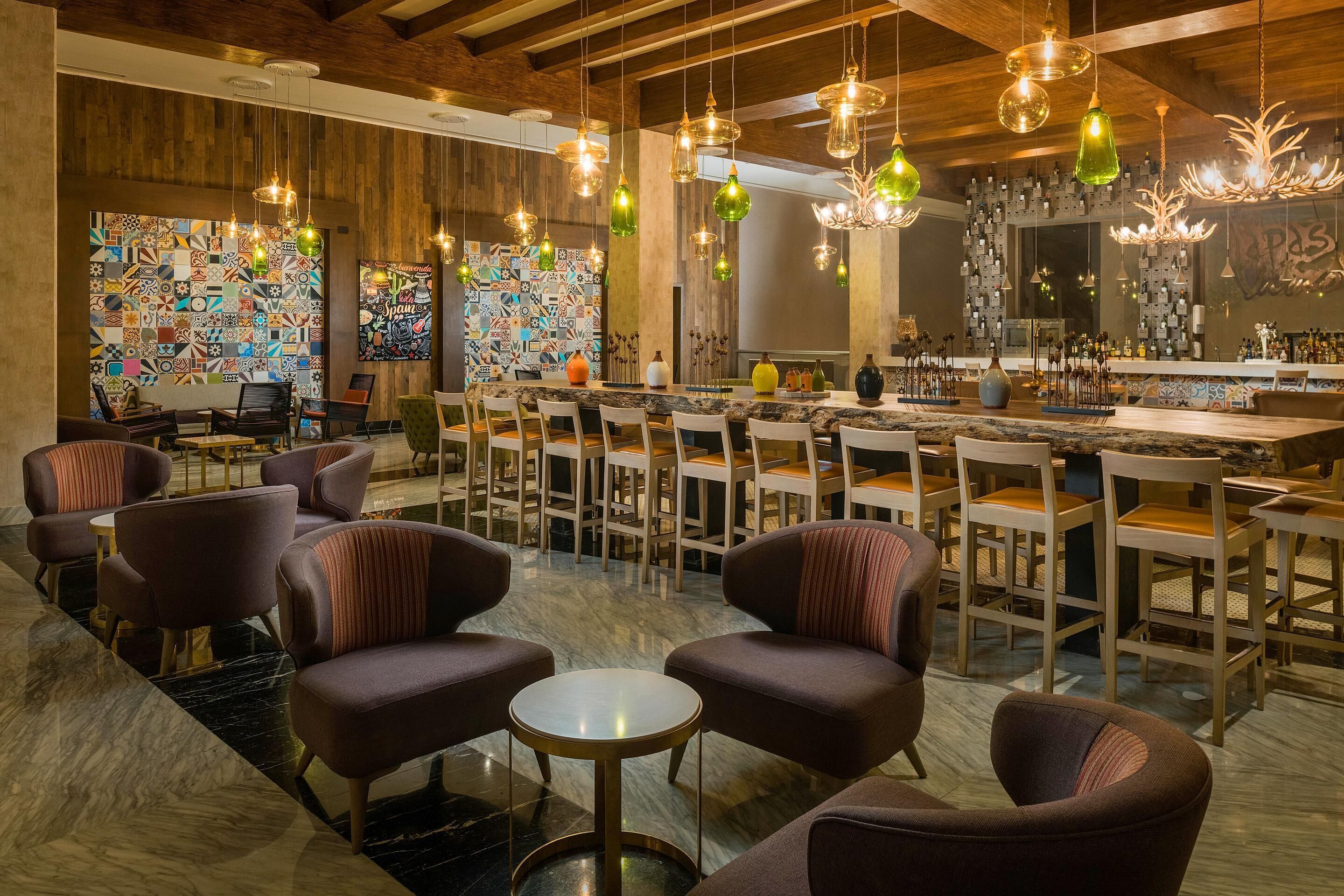 A modern bar area with multiple seating options, including bar stools and chairs, and a variety of hanging light fixtures.