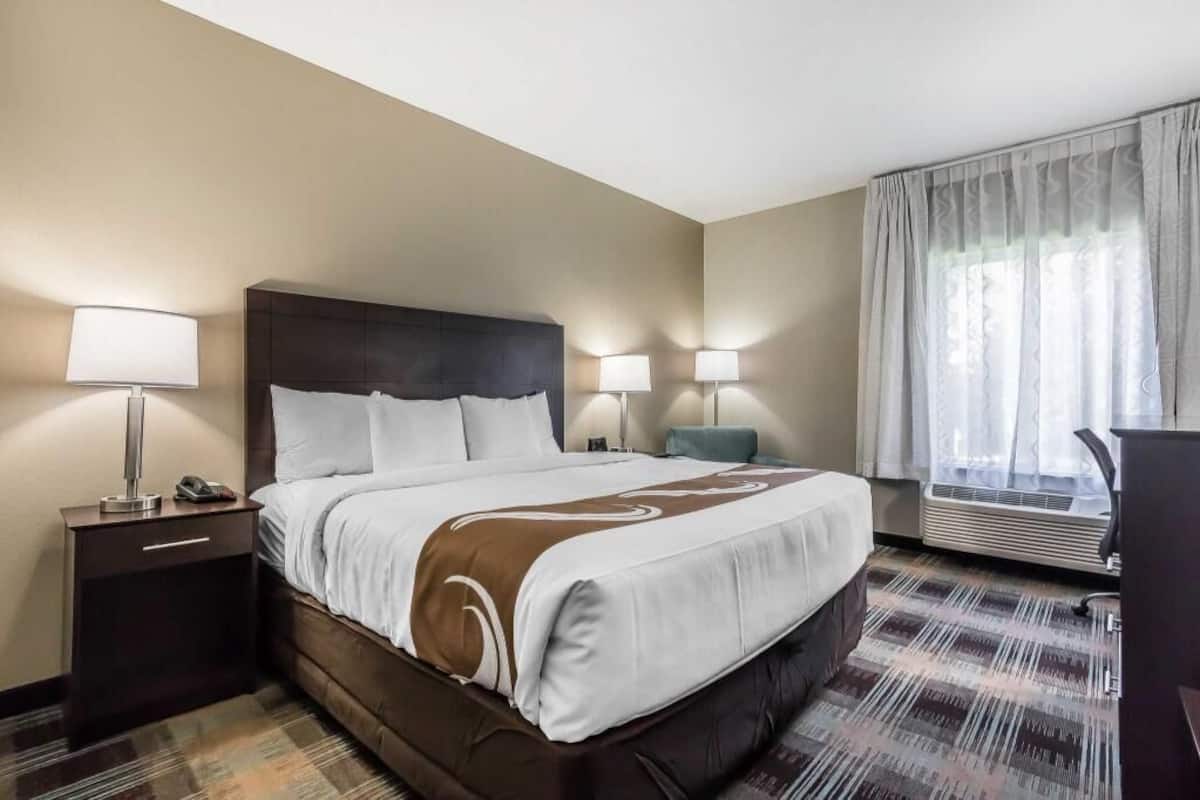 Ein Hotelzimmer mit einem großen Bett, Nachttischlampen, einem Schreibtisch und einem fenster mit Vorhängen.