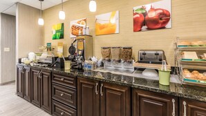 A hotel breakfast area with a counter, coffee machines, and a display case with pastries. - Quality Inn Pleasant View (Pleasant View)