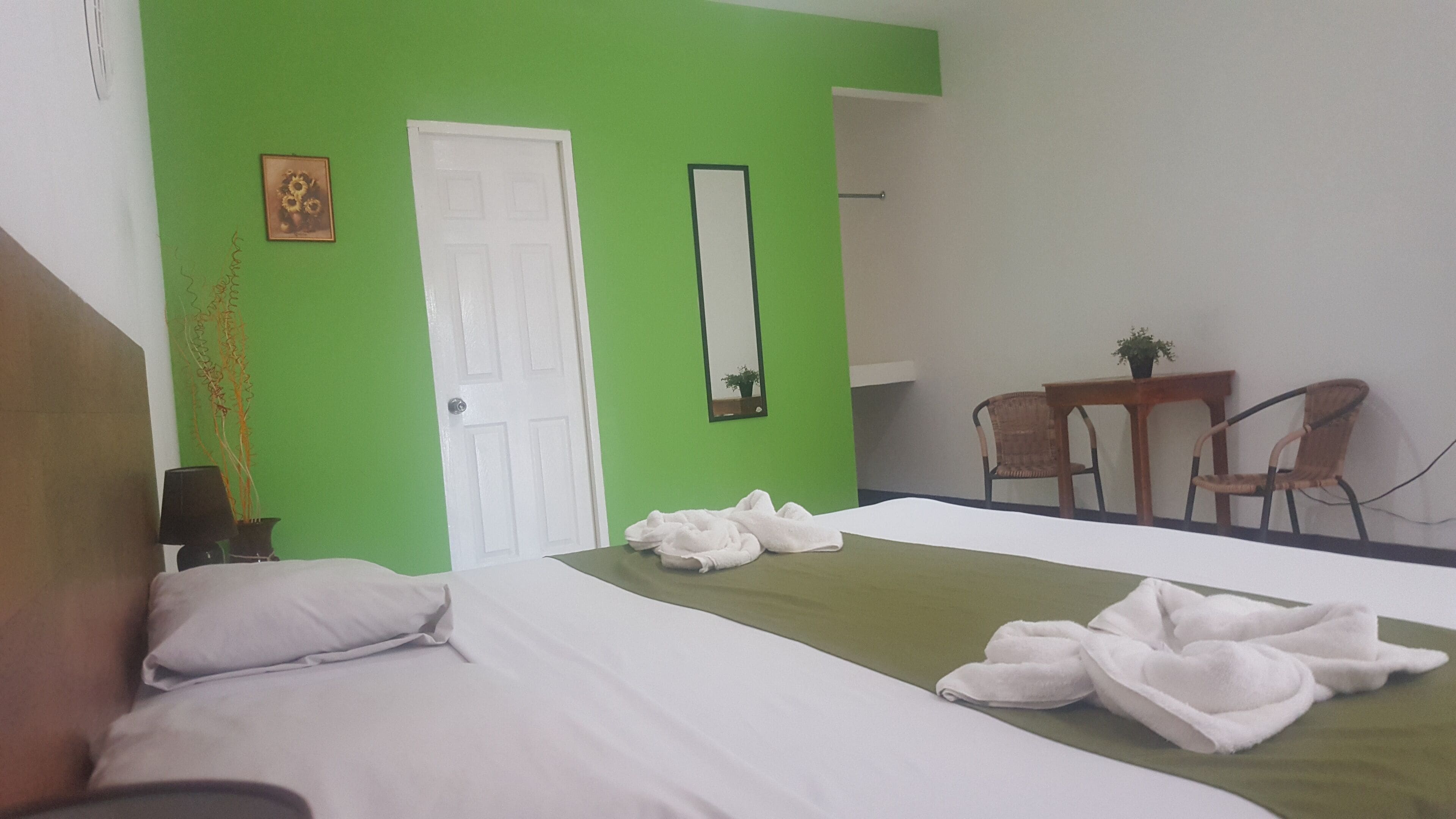 A hotel room with a bed, a desk, two chairs, a mirror, and a green wall.