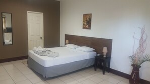 A hotel room with a bed, a nightstand, a lamp, a mirror, a door, and a painting on the wall. - Hotel La Arboleda (Managua)