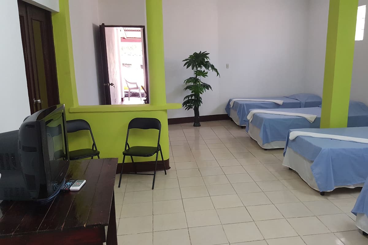 A room with a desk, two chairs, a television, and four beds with blue bedding.