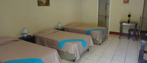 Habitación de hotel con tres camas, una mesita pequeña con una silla y una puerta que da a otra habitación.