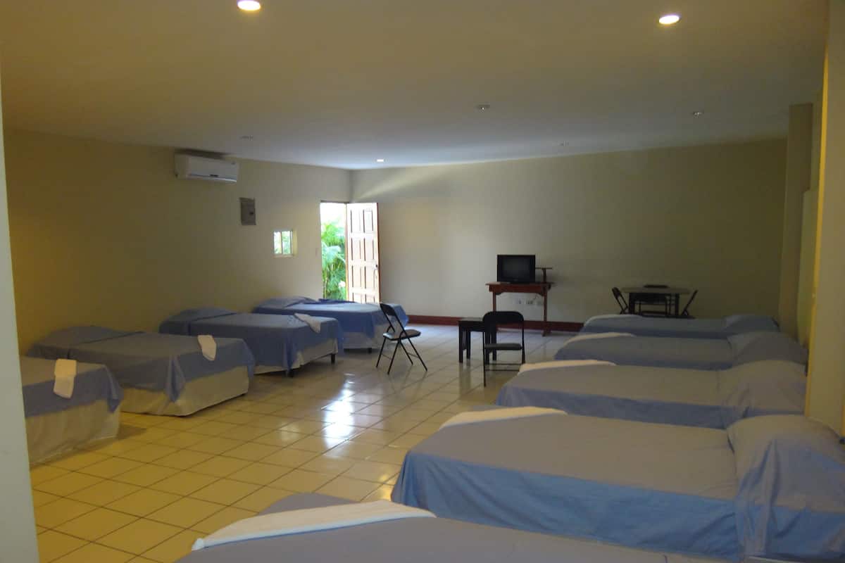 A hotel room with multiple beds, a television, a desk, and a chair.