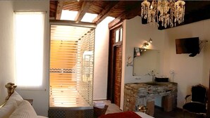Een slaapkamer met een groot bed, houten plafond, een wastafelmeubel van steen, een televisie en een kroonluchter.