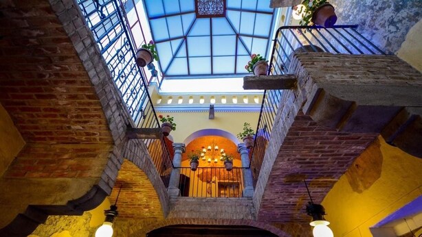 Een atrium met hoge plafonds, een dakraam, bakstenen muren en een centraal balkon met potplanten.