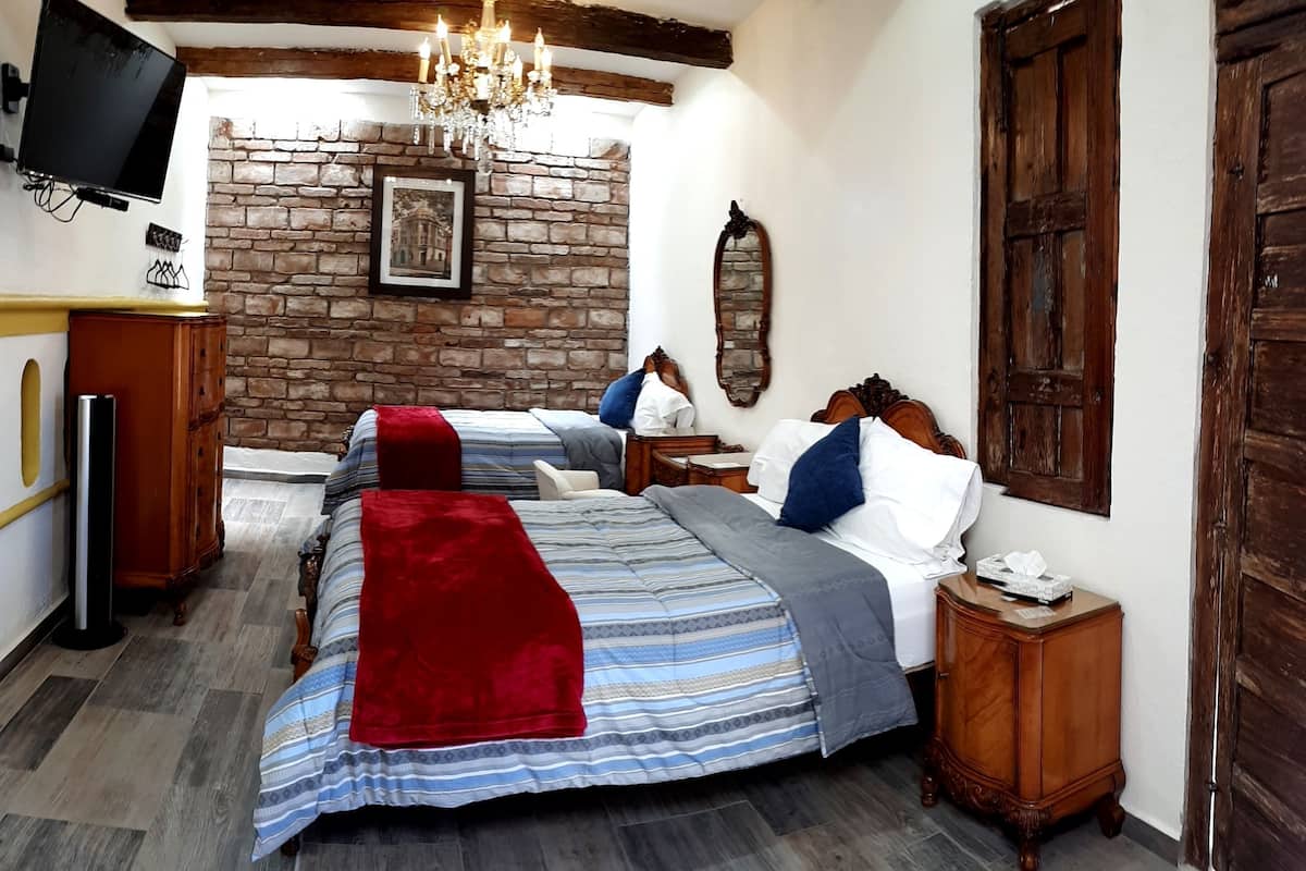 Een slaapkamer met twee bedden, een stenen muur, een kroonluchter en houten meubels.