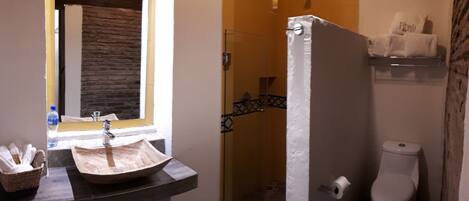 A bathroom with a stone wall, a sink, a shower, and a toilet.