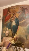 Een religieus schilderij met een figuur die een staf en een kroon vasthoudt, en een standbeeld met een vergelijkbare kroon en staf ervoor.