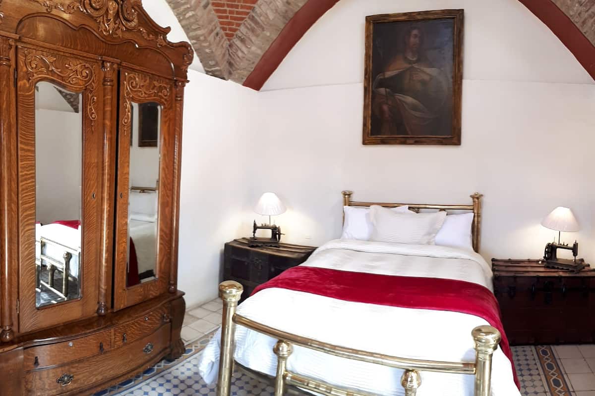 Een slaapkamer met een houten bed, twee nachtkastjes met lampen, een houten dressoir en een schilderij aan de muur.