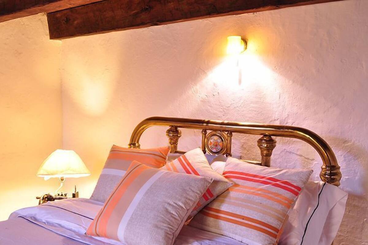 Een bed met een metalen hoofdbord, meerdere kussens en een bedlamp.
