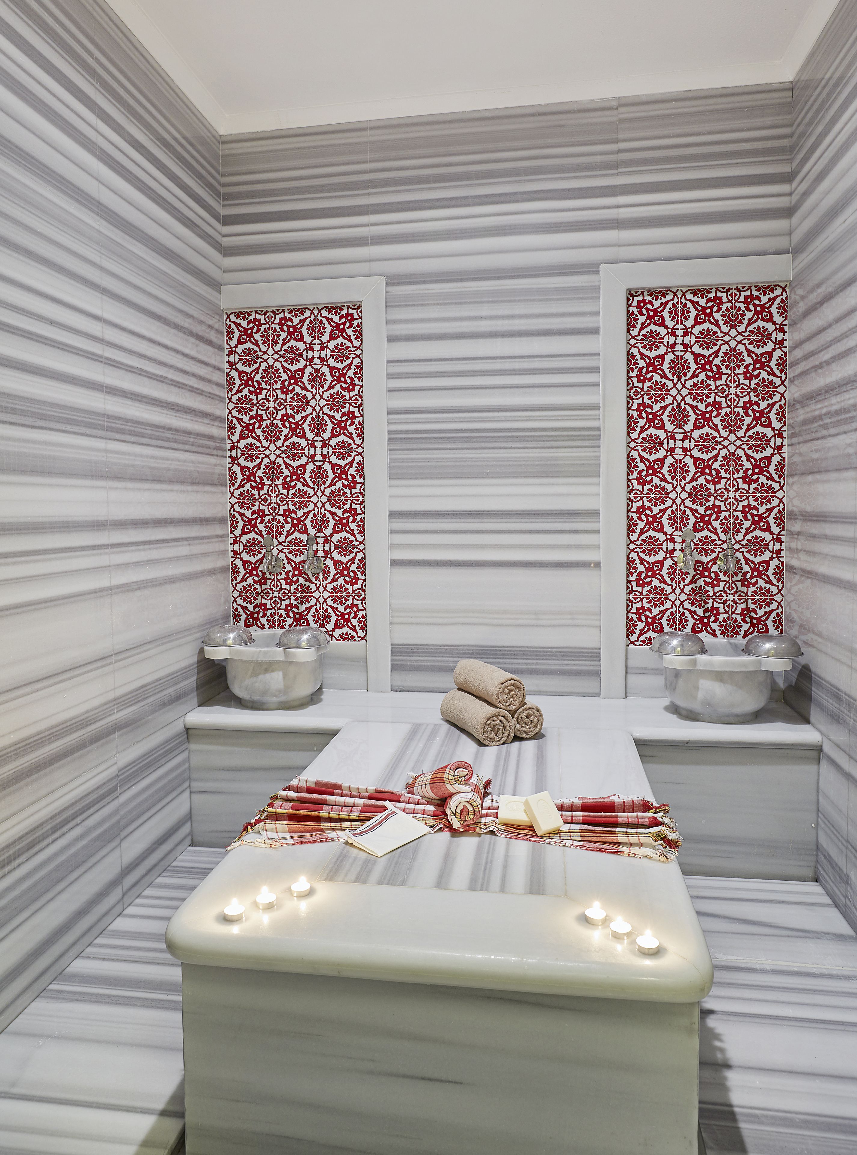 A spa room with a marble floor, a massage table, towels, and two sinks with decorative tiles.