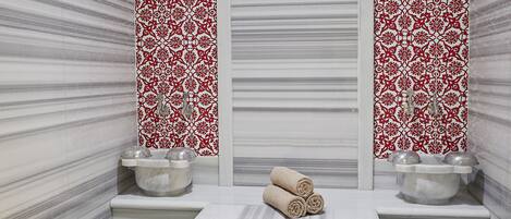 A spa room with a marble floor, a massage table, towels, and two sinks with decorative tiles.
