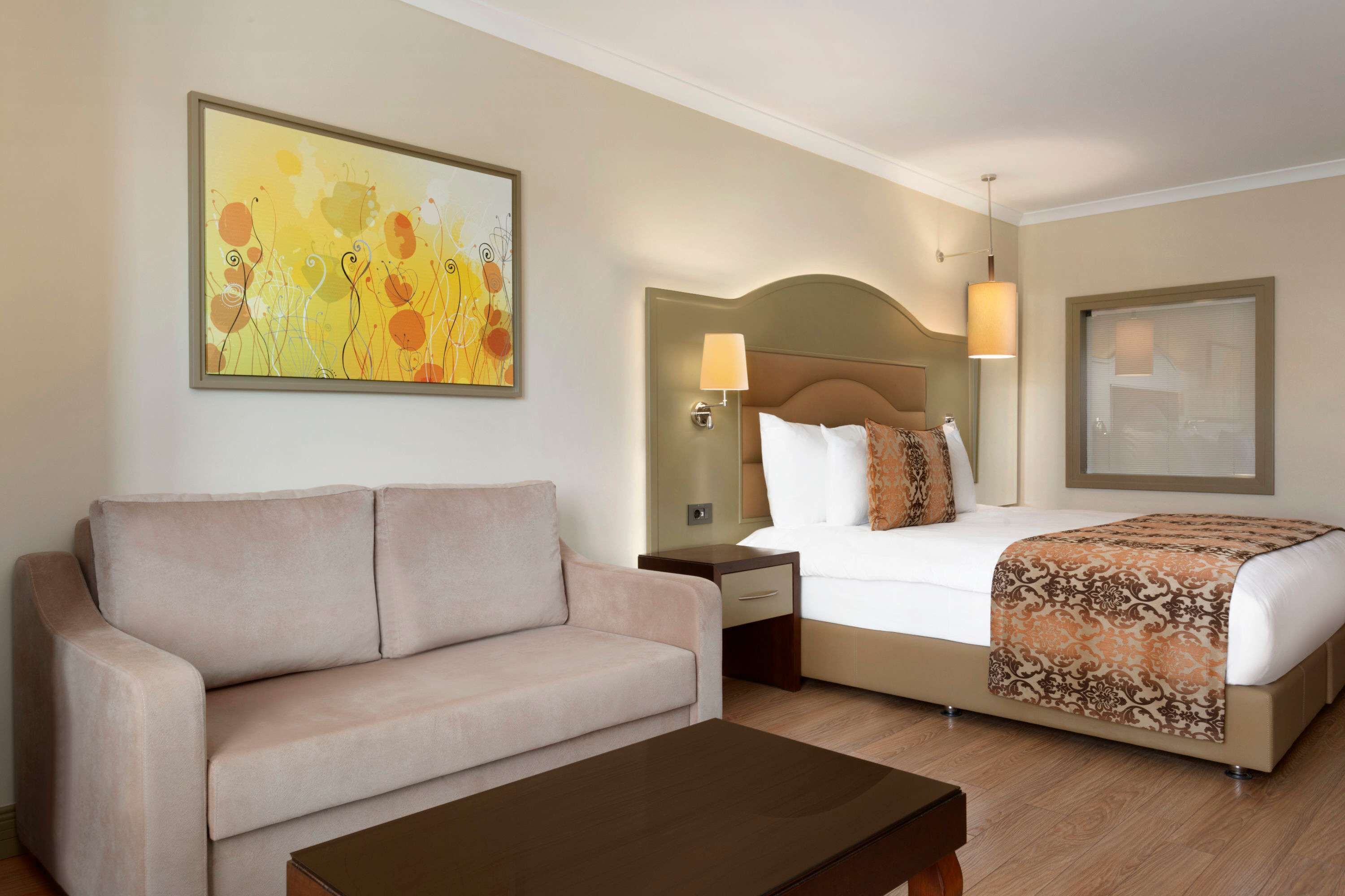 Una habitación de hotel con cama, sofá, mesita de noche, lámpara y un cuadro en la pared.