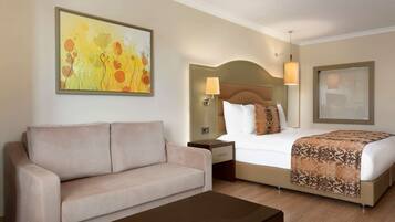 Una habitación de hotel con cama, sofá, mesita de noche, lámpara y un cuadro en la pared.