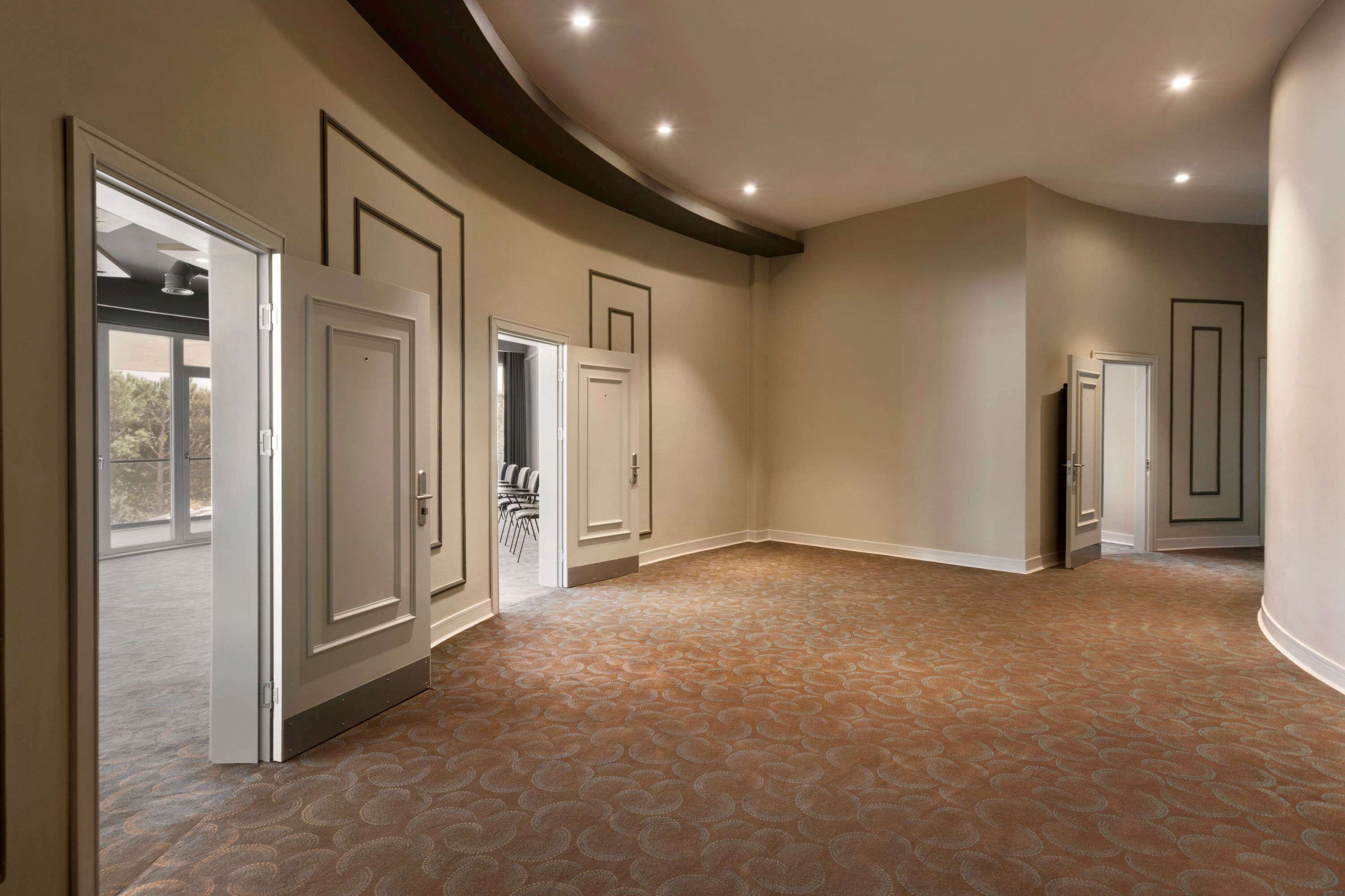 A spacious hallway with patterned carpet, multiple doors, and recessed ceiling lighting.