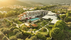 A hotel with a swimming pool, surrounded by landscaped gardens and a mountainous backdrop.