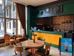 A cozy café with a green and yellow color scheme, featuring a round table with chairs, a coffee bar with a menu, and a large window with curtains. - Ramada Resort by Wyndham Kazdaglari Thermal and Spa (Edremit)