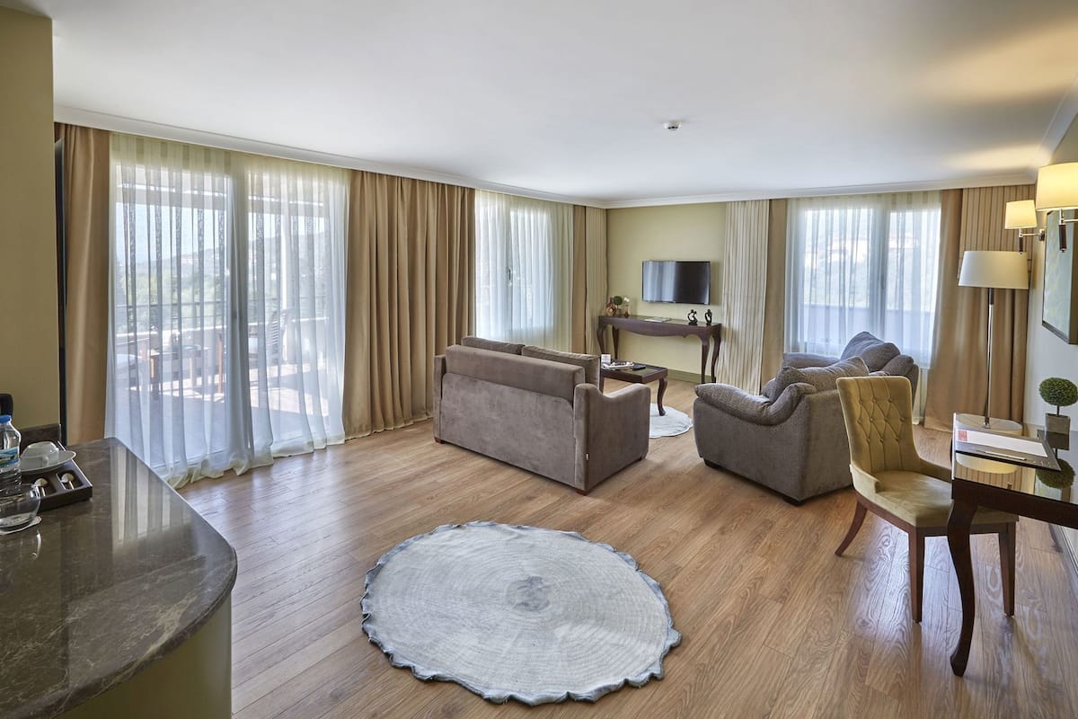 A hotel room with a sofa, armchair, dining table, and a TV.